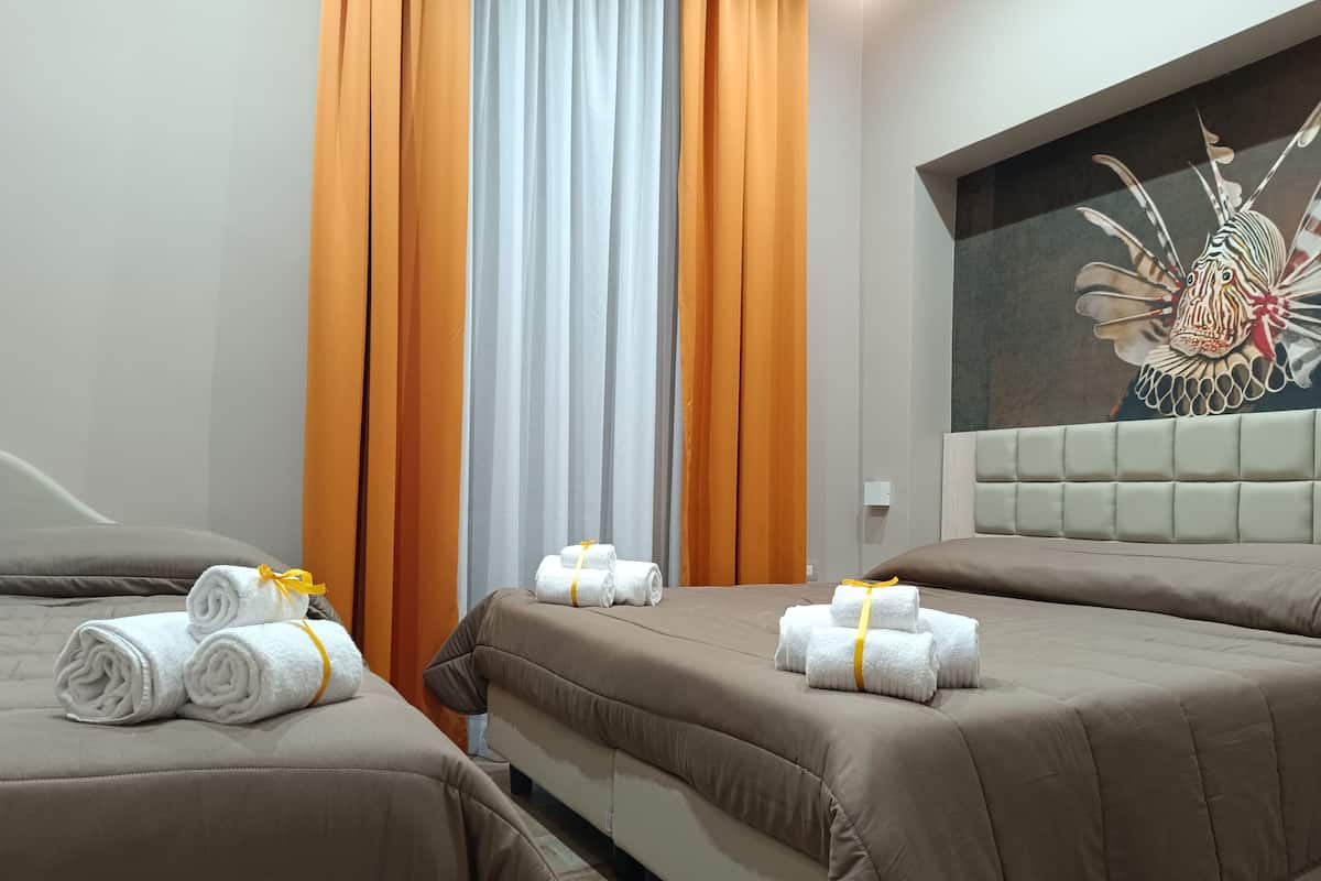 Habitación de hotel con dos camas, cada una adornada con toallas enrolladas y un lazo amarillo.