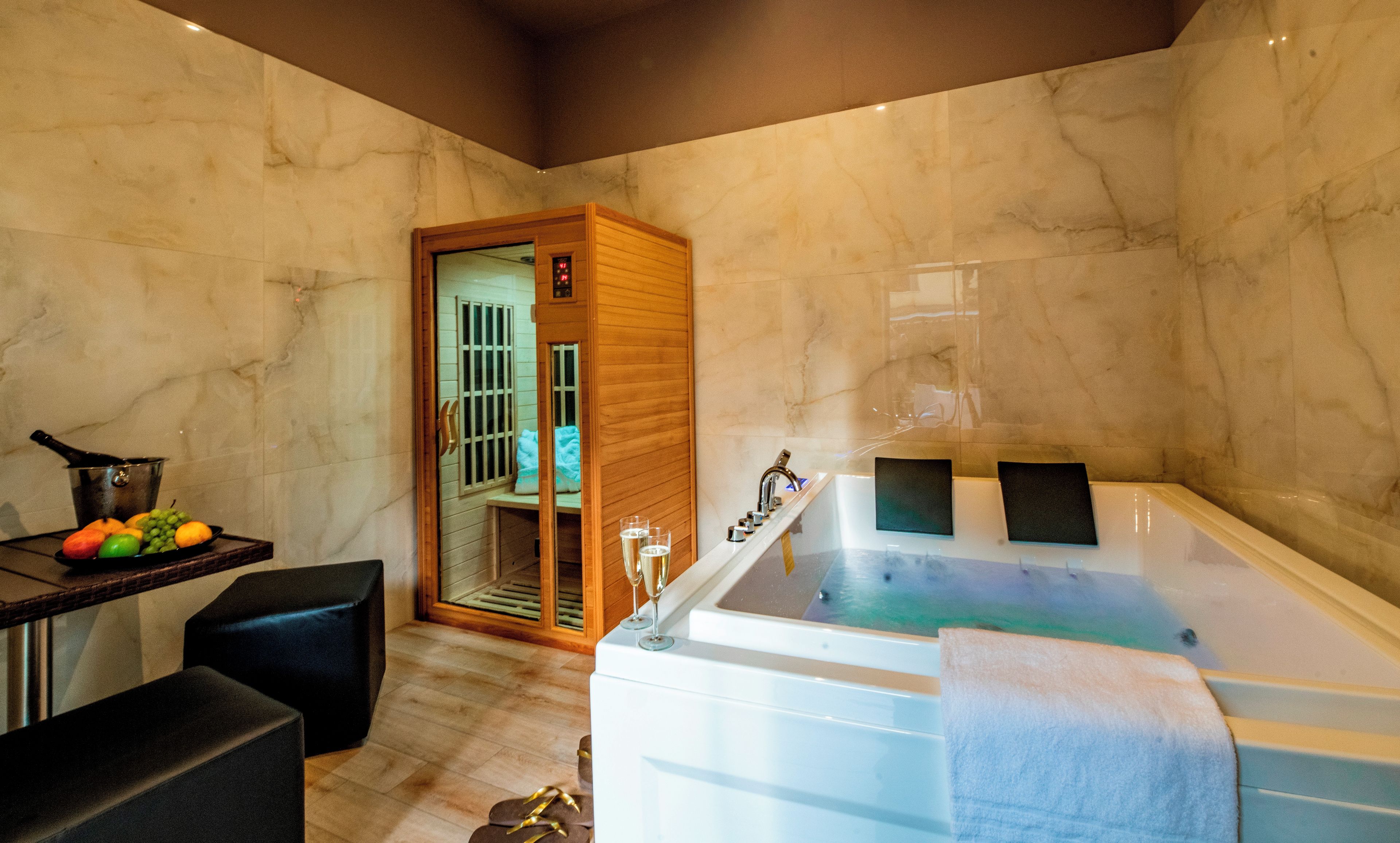 A modern bathroom with a marble wall, a bathtub, a wooden door, and a fruit bowl on a table.