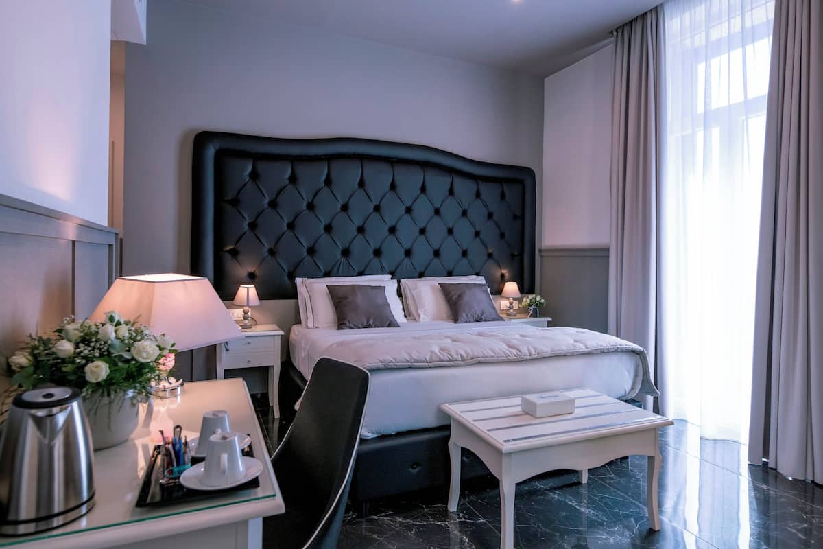 A hotel room with a large bed, bedside tables with lamps, a small desk, a chair, and a coffee maker.