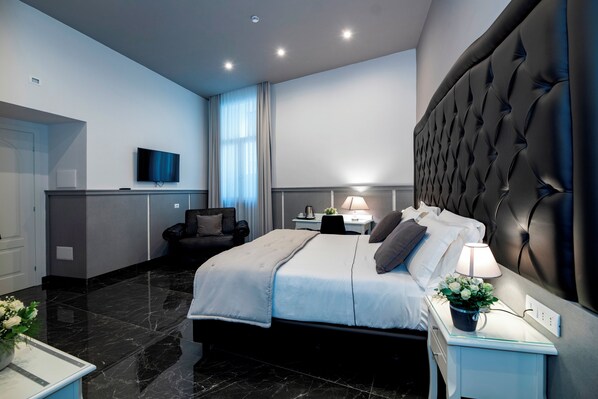 A modern bedroom with a large bed, a flat-screen TV, a desk, and a chair.