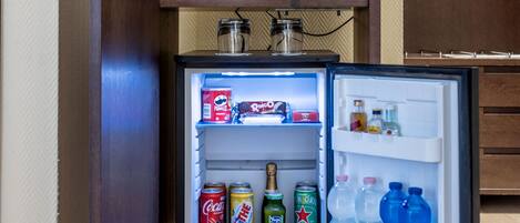 Un refrigerador compacto con minibar integrado, que contiene diversas bebidas y aperitivos.
