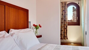 A bedroom with a wooden headboard, a bed with white linens, a vase with red flowers, and a view of a historic building through an arched window. - Due Mori (Marostica)