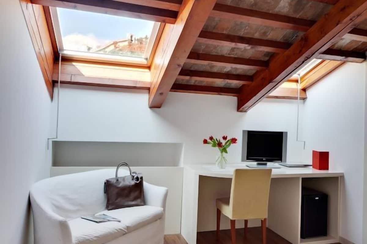 Habitación pequeña con techo inclinado, una cama, un escritorio con computadora y una ventana.