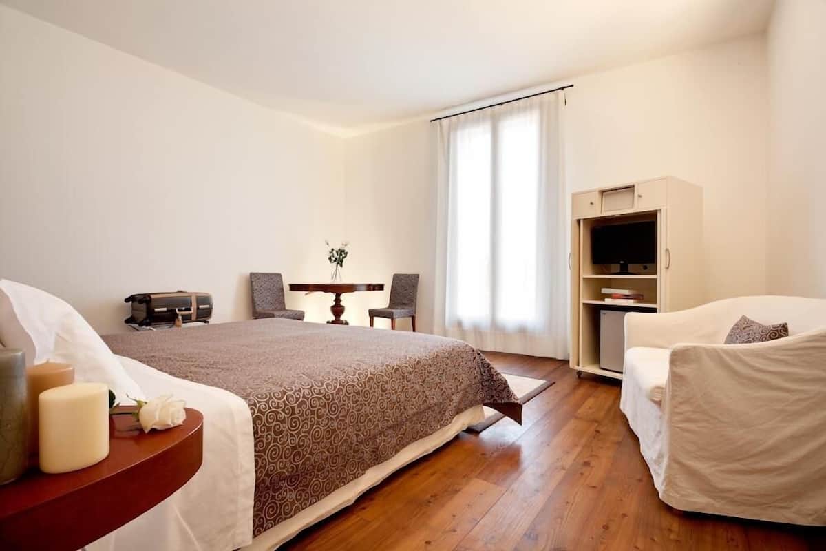 Una habitación de hotel con cama, mesita de noche, silla, escritorio y mueble para televisión.