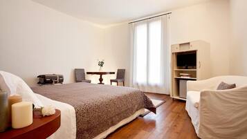 Quarto de hotel com cama, mesa de cabeceira, cadeira, escrivaninha e um suporte para televisão.