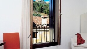 A hotel room with a bed, a red chair, a dining table with breakfast items, and a view of a mountainous landscape through an open window. - Due Mori (Marostica)
