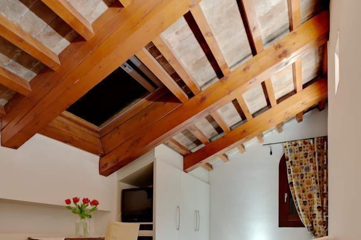 Un dormitorio acogedor en el ático, con techo de madera, un escritorio pequeño con silla, una cama y un televisor en una esquina.