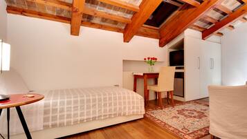Una habitación compacta con cama, una mesita, una silla, un escritorio y una kitchenette.