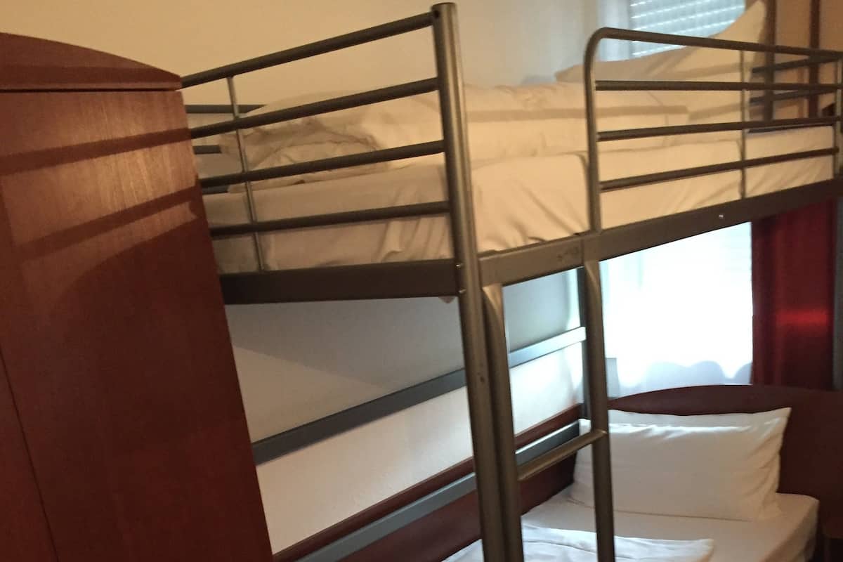Een slaapkamer met een stapelbed, een houten garderobe en een raam met gordijnen.