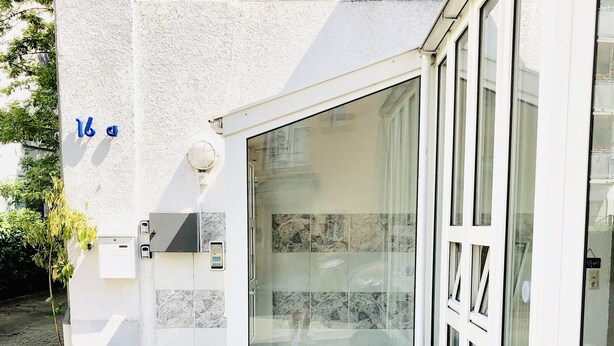 A modern building with a glass door, a small garden area with artificial grass, and a decorative yellow vase. - Hotel Aurelia (Frankfurt)