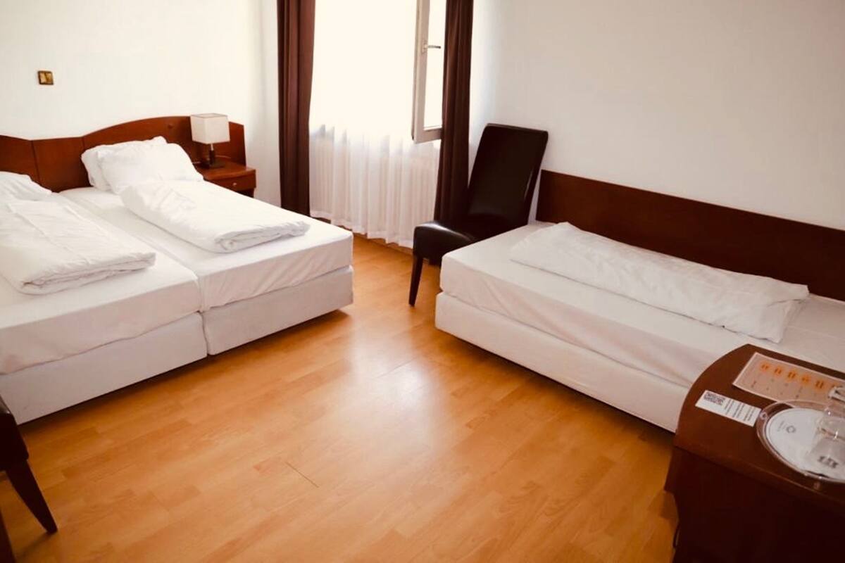 Een hotelkamer met twee bedden, een stoel, een nachtkastje en een raam met gordijnen.