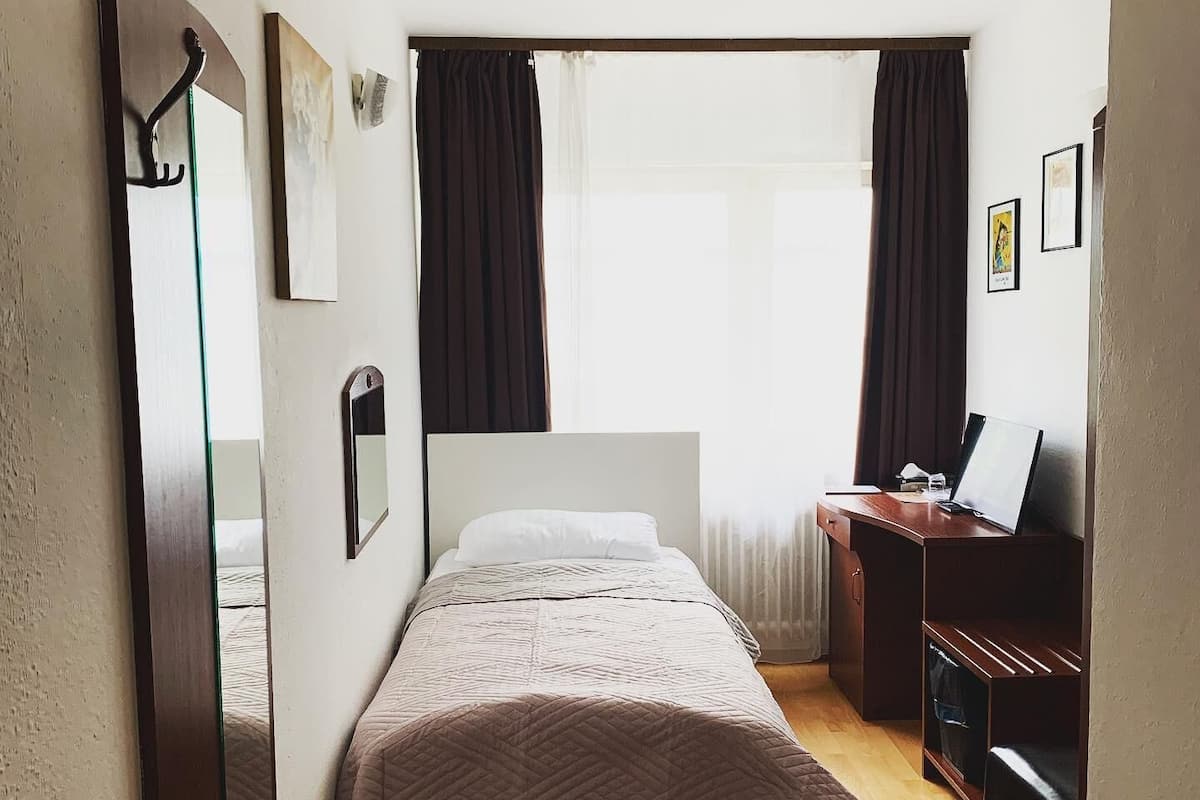 Een slaapkamer met een bed, een bureau, een stoel, een spiegel en een raam met gordijnen.