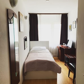 A bedroom with a bed, a desk, a chair, a mirror, and a window with curtains.