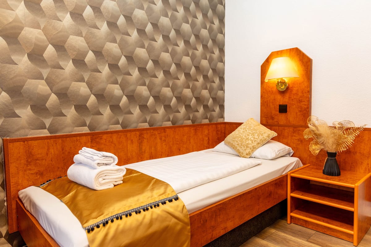 A neatly made bed with folded towels, a bedside lamp, and a decorative vase on a wooden nightstand.
