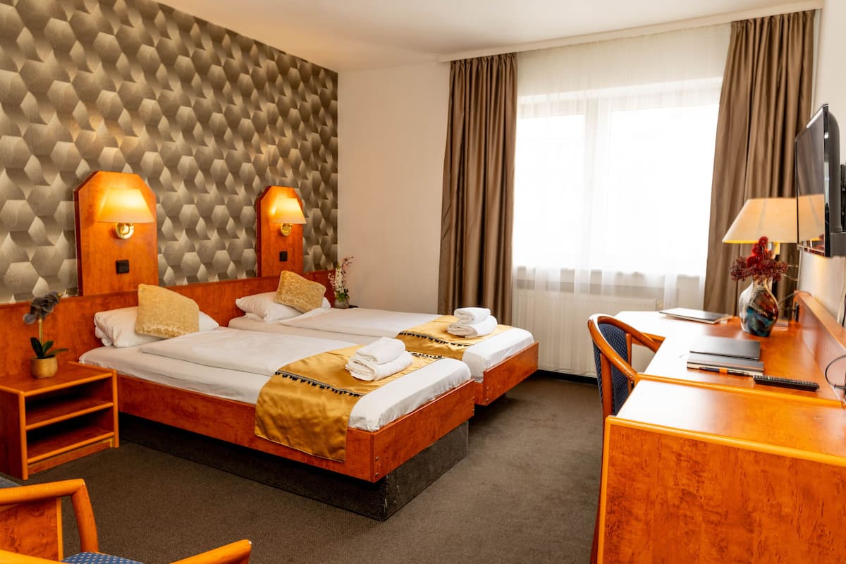 A hotel room with two beds, a desk, a chair, a TV, and a wall with a geometric pattern.