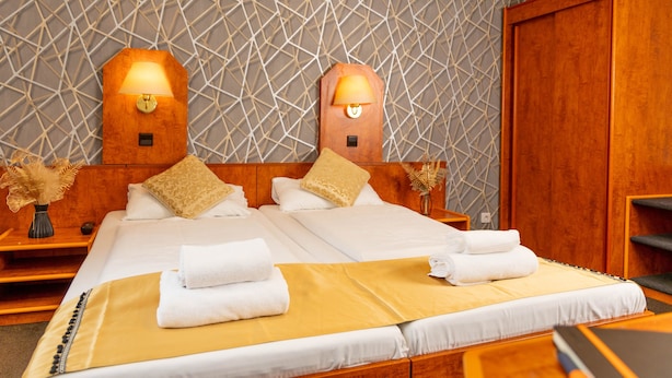Habitación de hotel con una cama grande, dos mesitas de noche, un armario de madera y un papel tapiz con estampado geométrico.