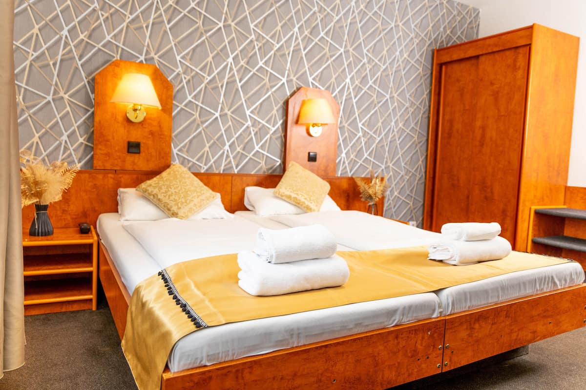A neatly made bed with white linens and a yellow accent, two bedside lamps, and a geometric patterned wall.