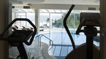Espaço de exercícios interno com vista para uma piscina ao ar livre e uma praia.
