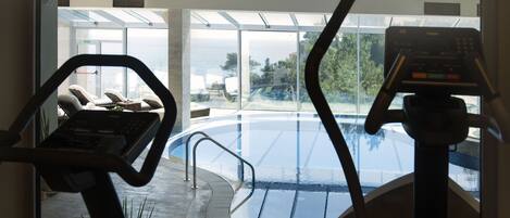 An indoor exercise area with a view of an outdoor swimming pool and a beach.