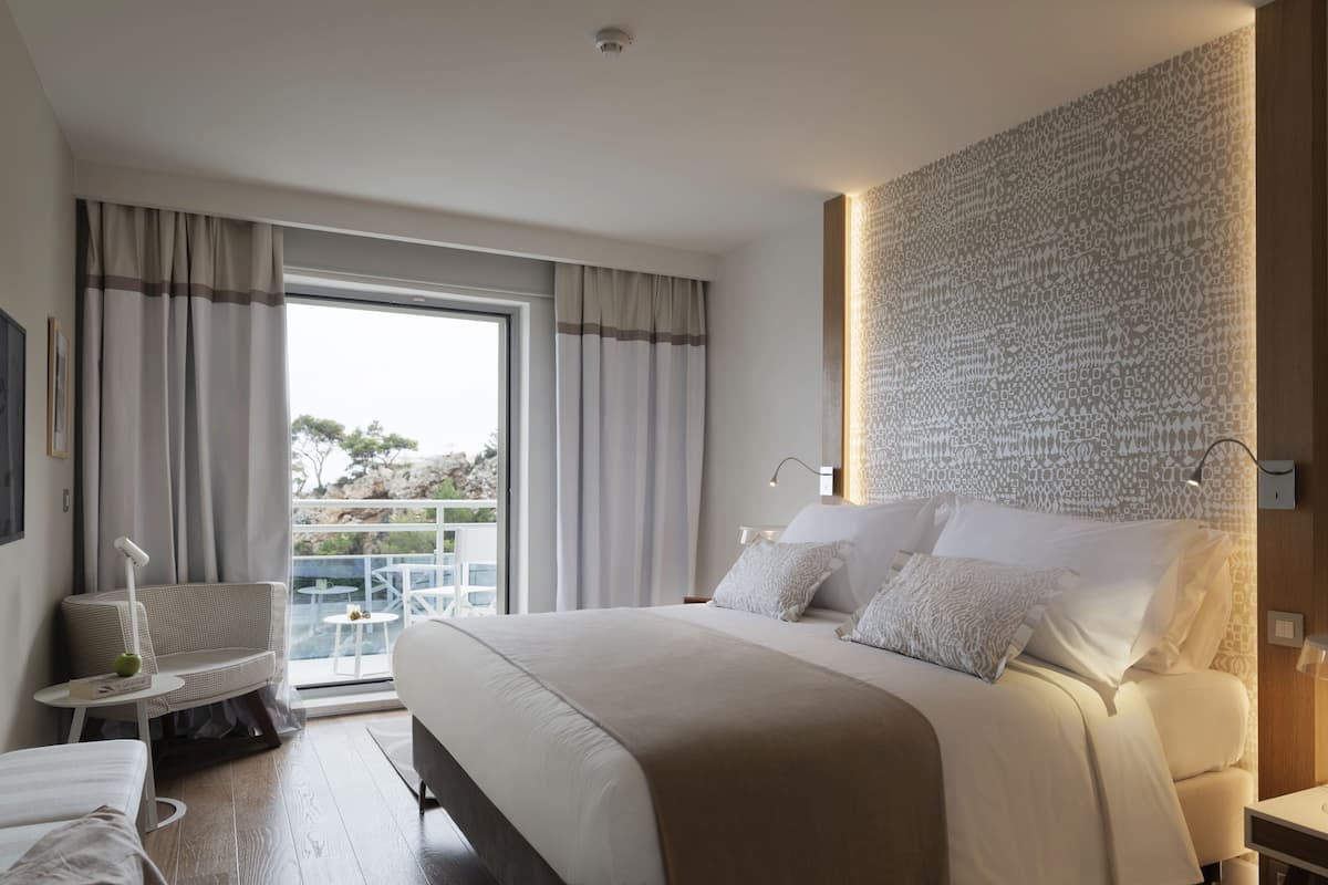 Une chambre d’hôtel moderne avec un grand lit, un balcon offrant une vue agréable et un mur décoré de motifs.
