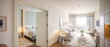 A modern hotel room with a bed, a sofa, a small table, and a balcony with a view.