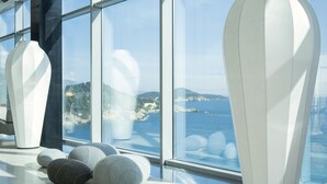 Een modern interieur met grote ramen, uitzicht op zee en verschillende grote vazen op een gepolijste vloer.