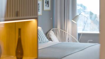 A modern bedroom with a bed, bedside lamp, and a view of mountains through a window.