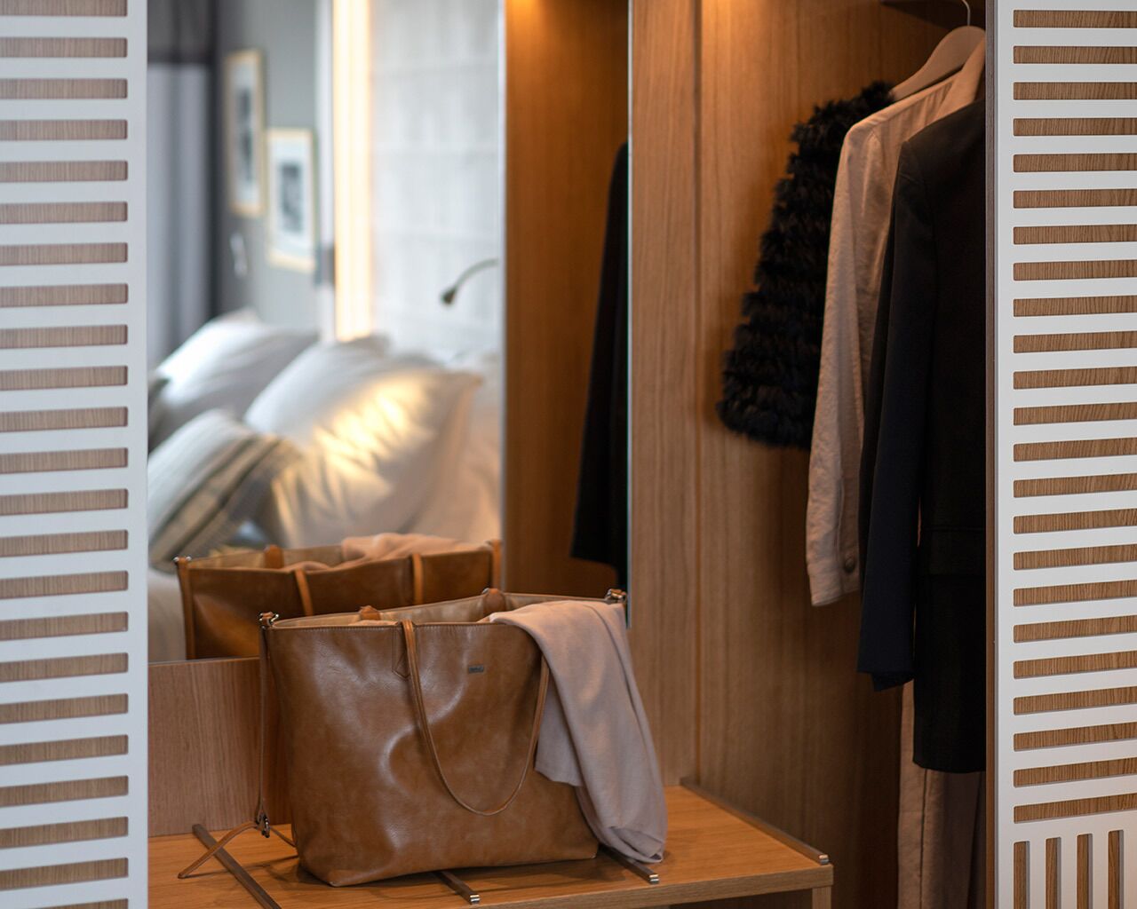 A room with a bed, a wooden wardrobe, and a table with a brown leather bag and a grey cloth.