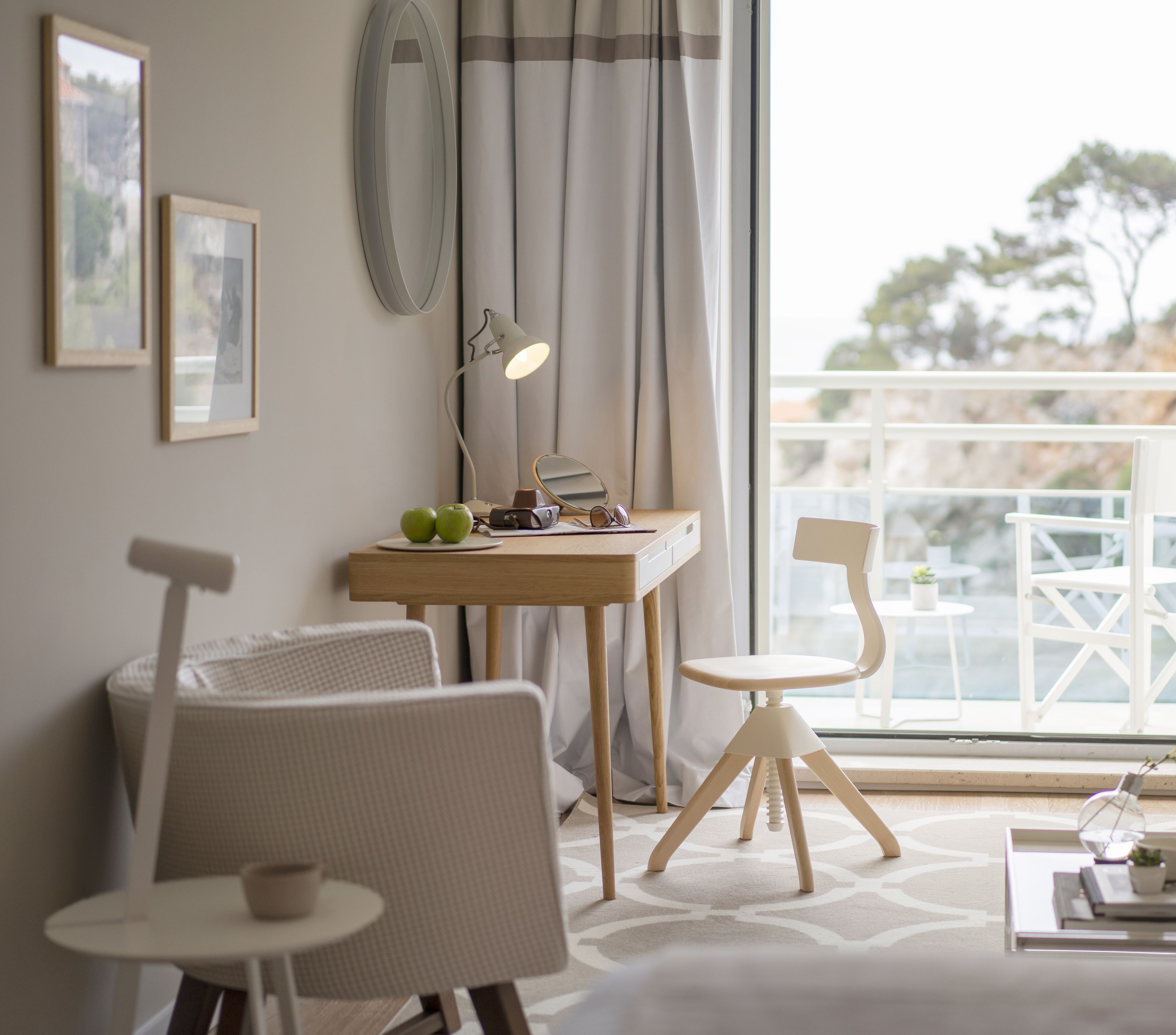 A modern room with a desk, two chairs, a small table, a lamp, and a view of the outdoors.