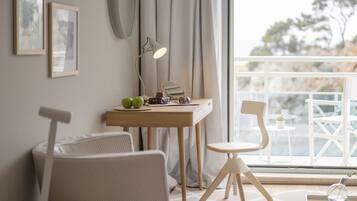 A modern room with a desk, two chairs, a small table, a lamp, and a view of the outdoors.