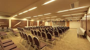 A conference room with rows of chairs, a stage with lighting, and a carpeted floor.