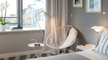 Una habitación de hotel moderna con una cama, una silla blanca, una mesita con una planta, una lámpara y una ventana con cortinas.