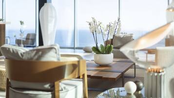Een moderne woonkamer met een groot raam, een witte vaas met witte bloemen, een houten salontafel en een bank met kussens.