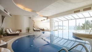 Een groot binnenzwembad met loungegedeeltes, een uitzicht op zee en een modern architectonisch ontwerp.