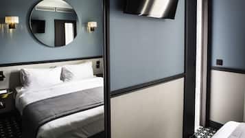 A hotel room with a bed, a round mirror, a flat-screen TV, and a wall-mounted light fixture.