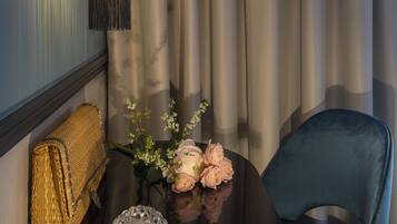 A room with a round black table, a blue chair, a lamp, a woven basket, and a vase with flowers.