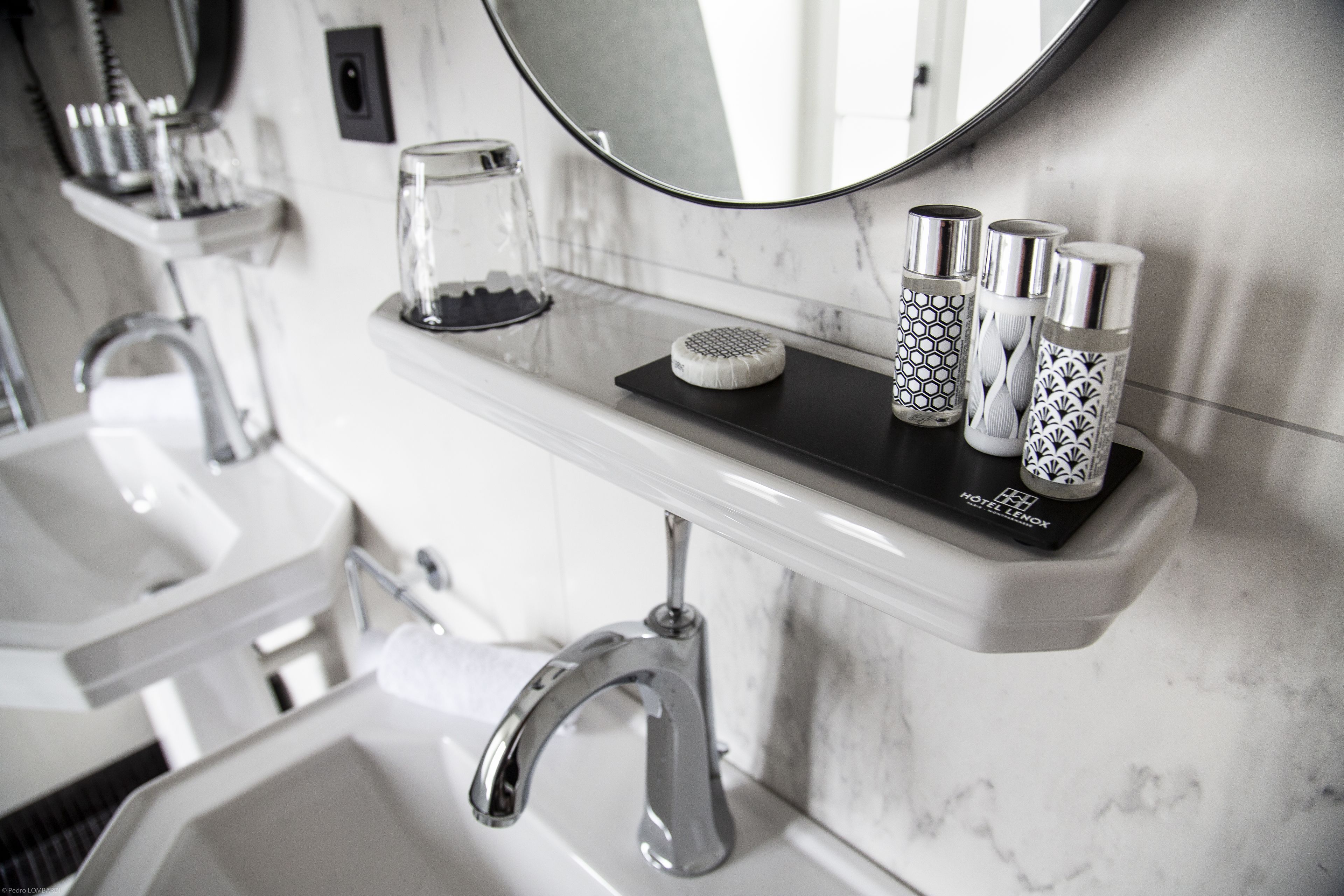 Une salle de bain moderne avec un comptoir en marbre, un miroir rond et une étagère contenant des articles de toilette.