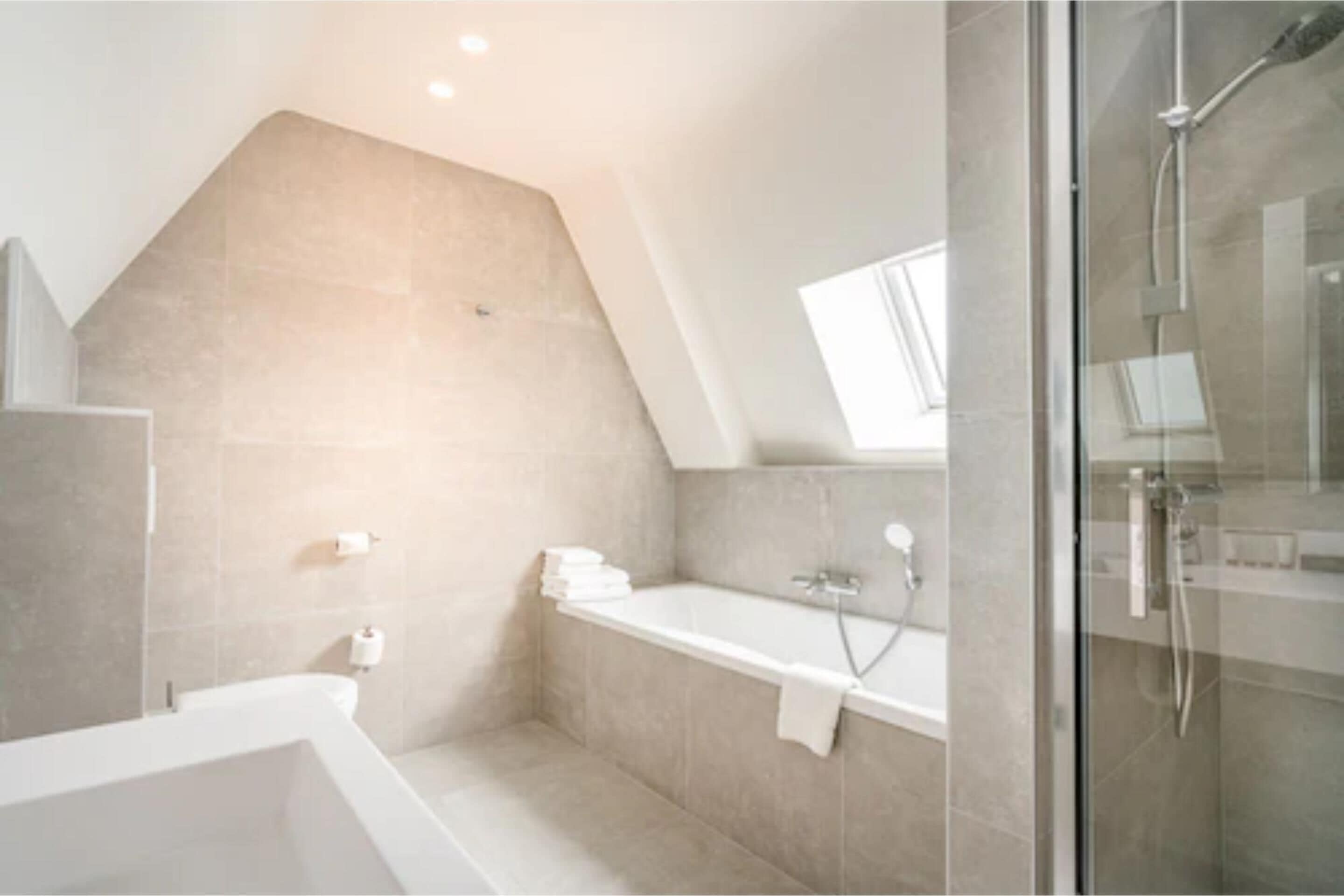 Une salle de bain moderne avec une baignoire sur pieds, une douche à parois de verre et un puits de lumière.