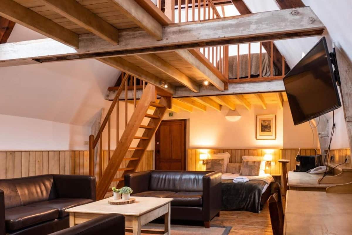 A cozy loft-style room with a wooden staircase, a sofa, a coffee table, and a TV mounted on the wall.
