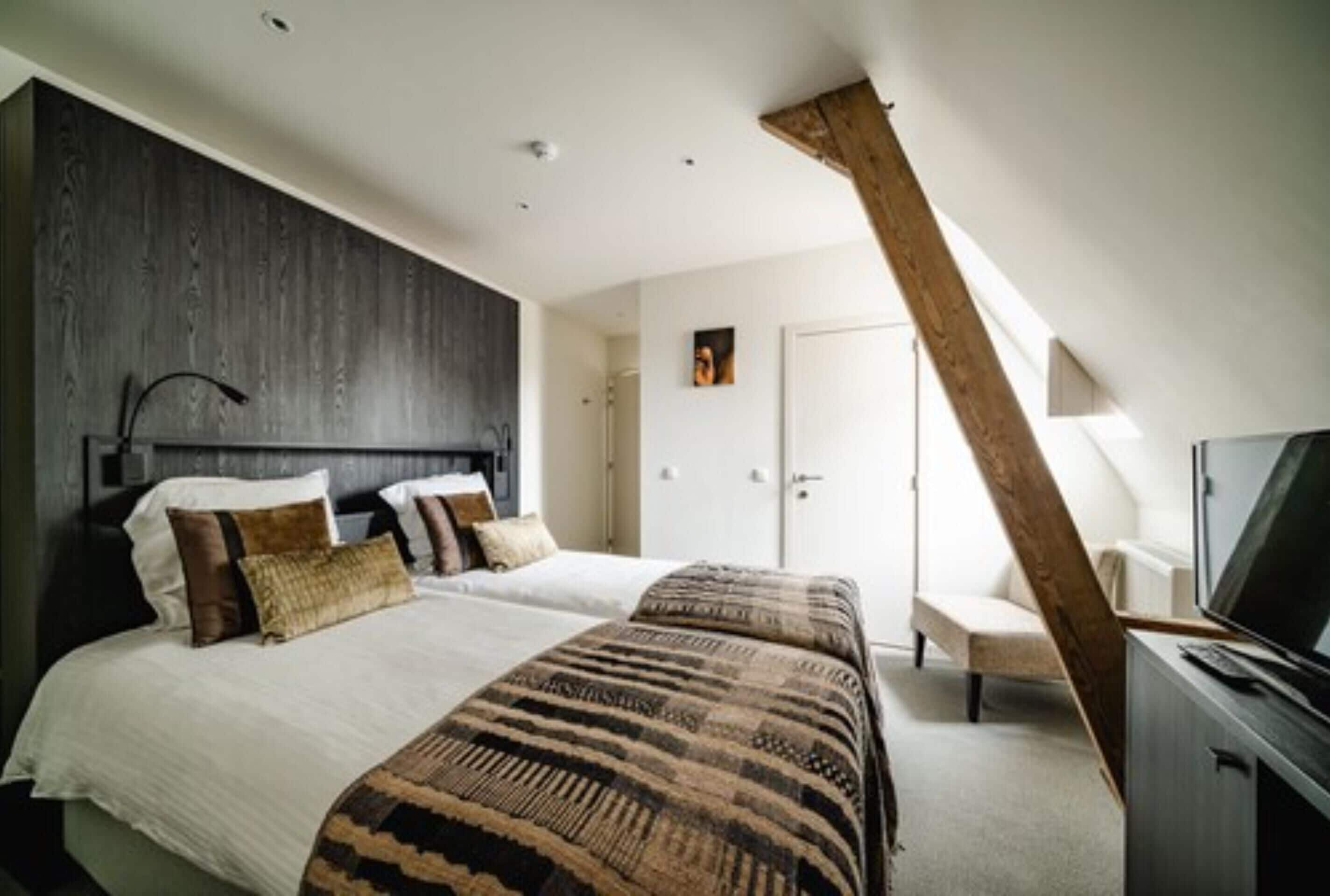 Une chambre avec un grand lit, une poutre en bois au plafond, une télévision et une porte.