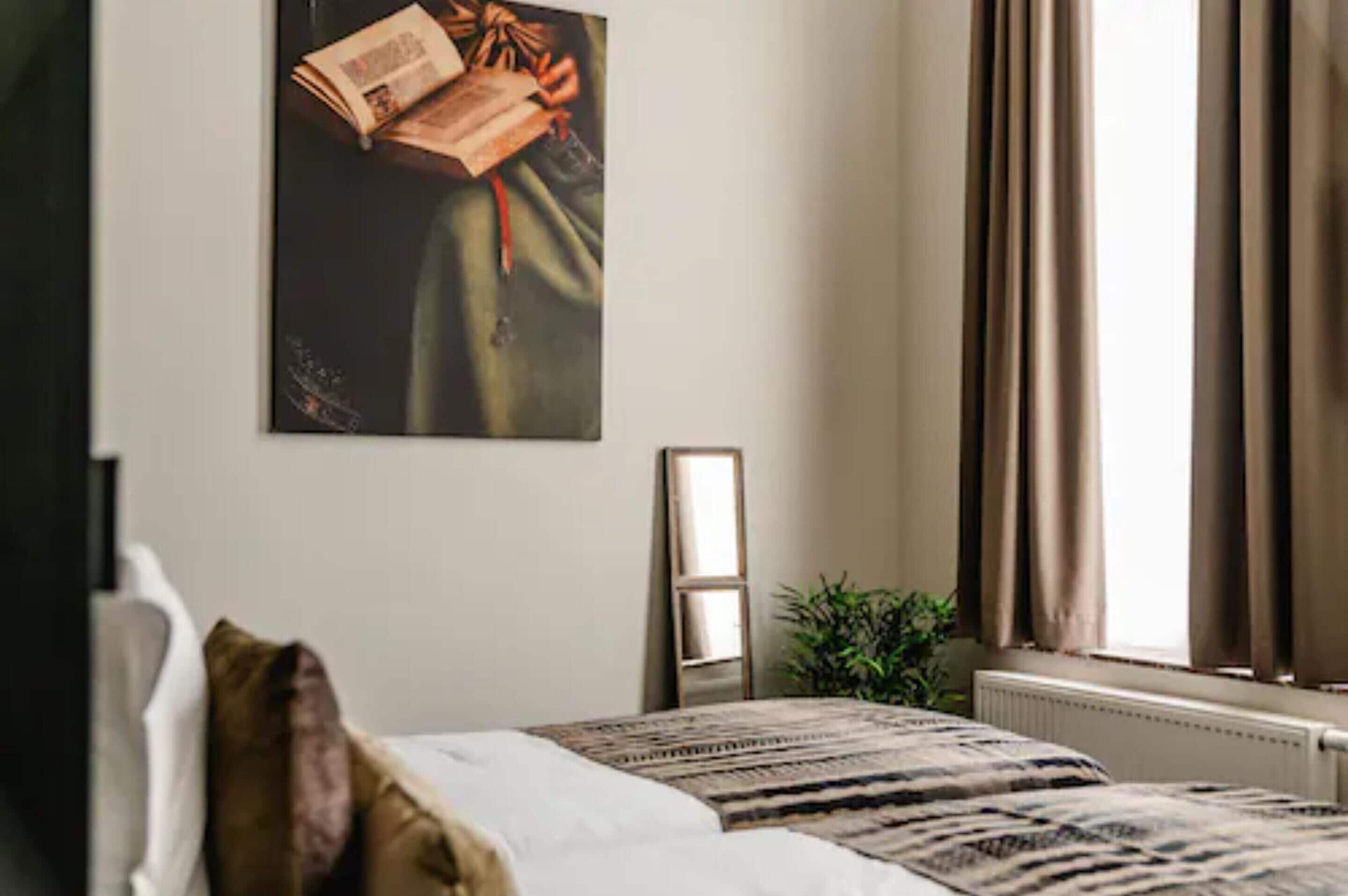 Habitación de hotel con una cama, un espejo, una ventana con cortinas y un cuadro en la pared.