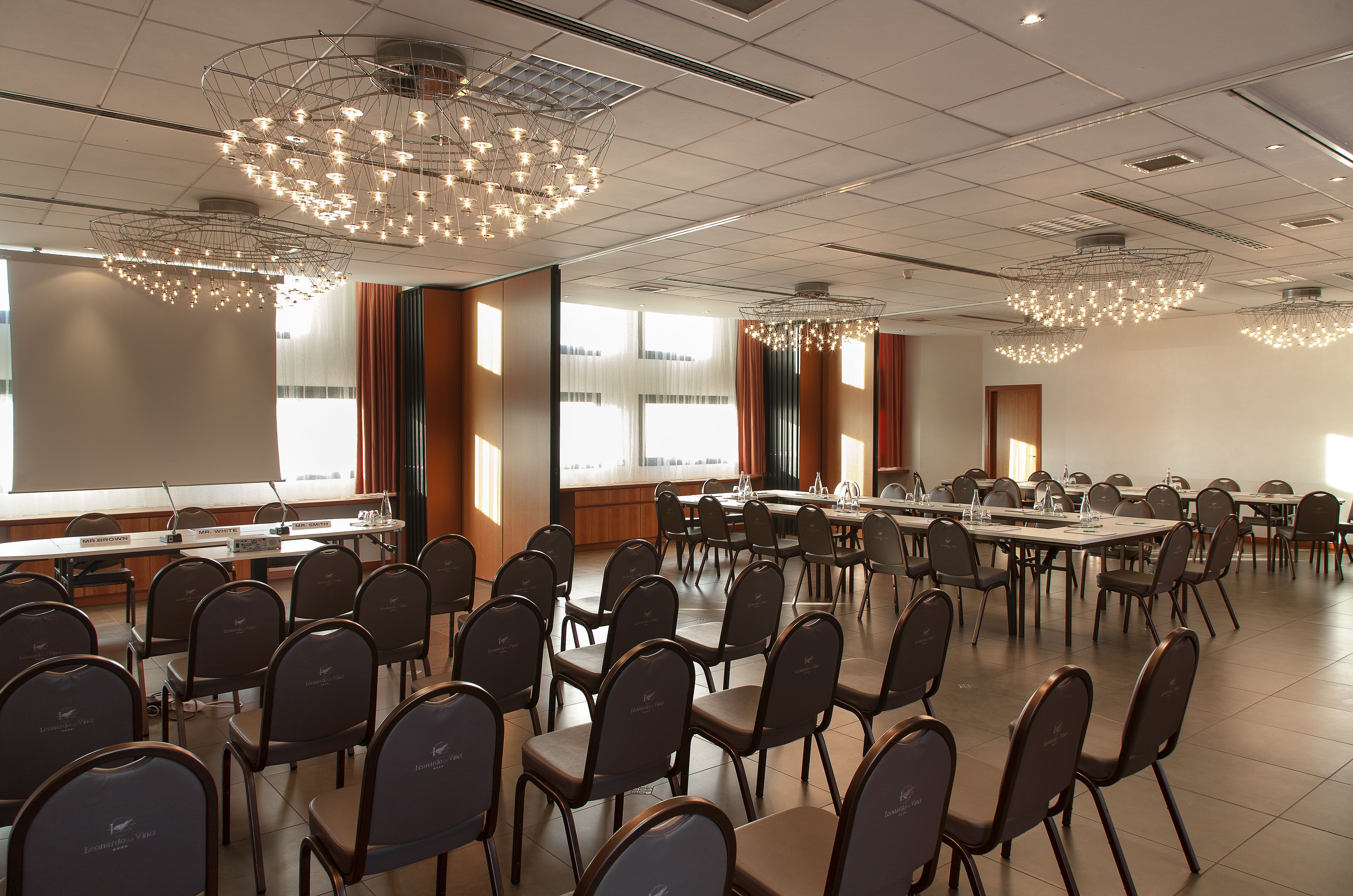 A conference room with rows of chairs, tables, and a large screen.