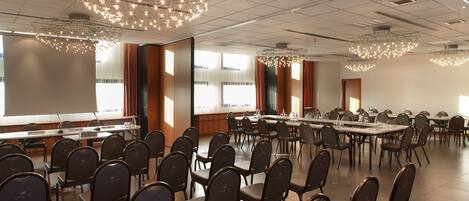 Un salón de conferencias con filas de sillas, mesas y una pantalla grande.