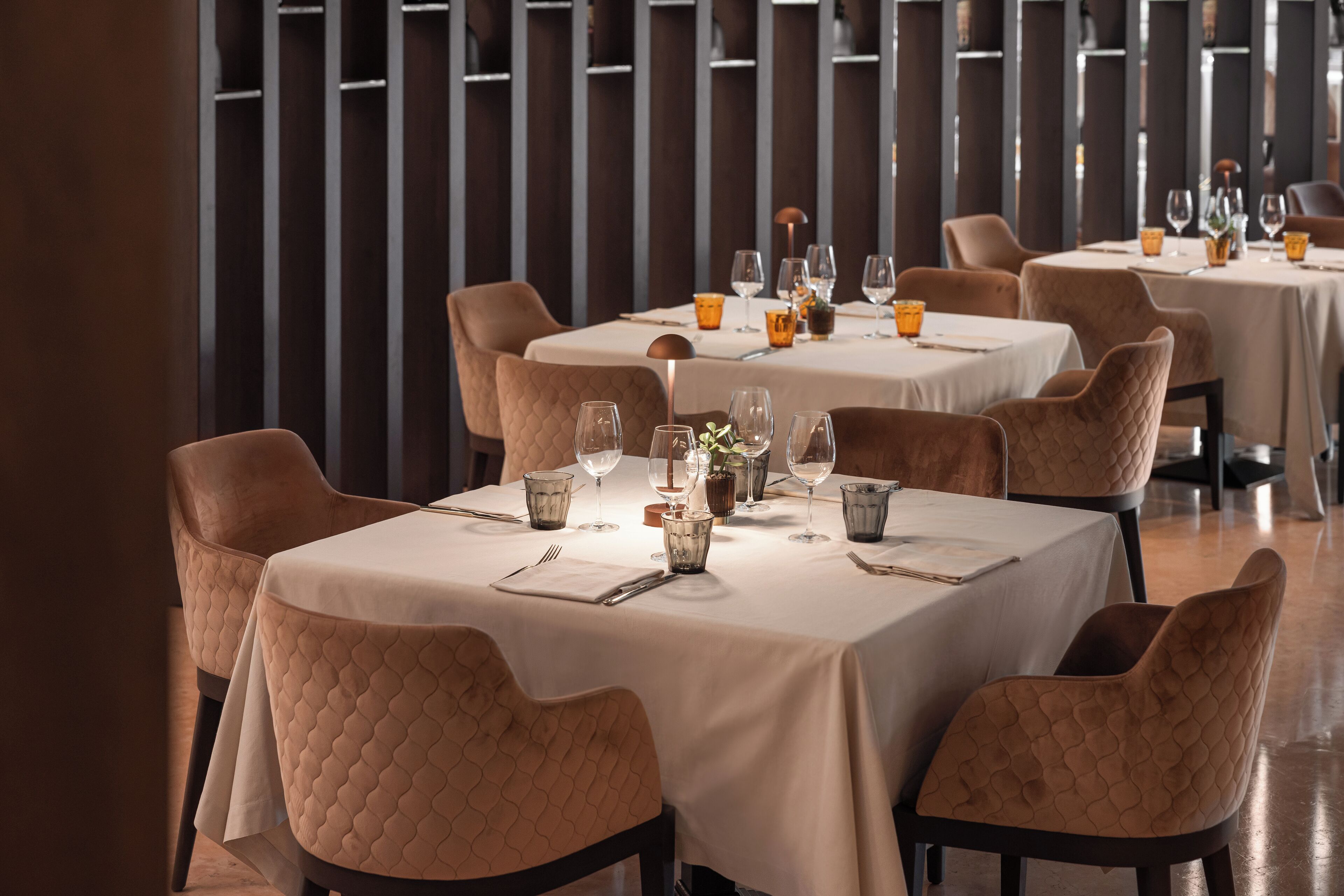 Restaurante com mesas postas para refeições, cadeiras acolchoadas e design de interiores moderno.