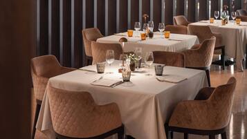 Restaurante com mesas postas para refeições, cadeiras acolchoadas e design de interiores moderno.