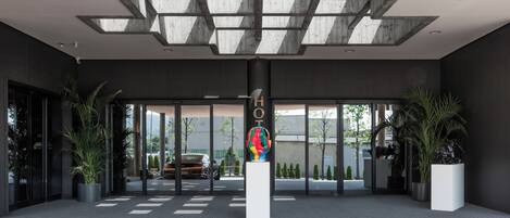 A modern hotel entrance with a geometric ceiling design, large glass doors, and potted plants.