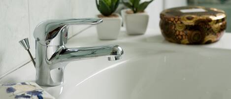 A bathroom sink with a chrome faucet, a small potted plant, and a decorative bowl.