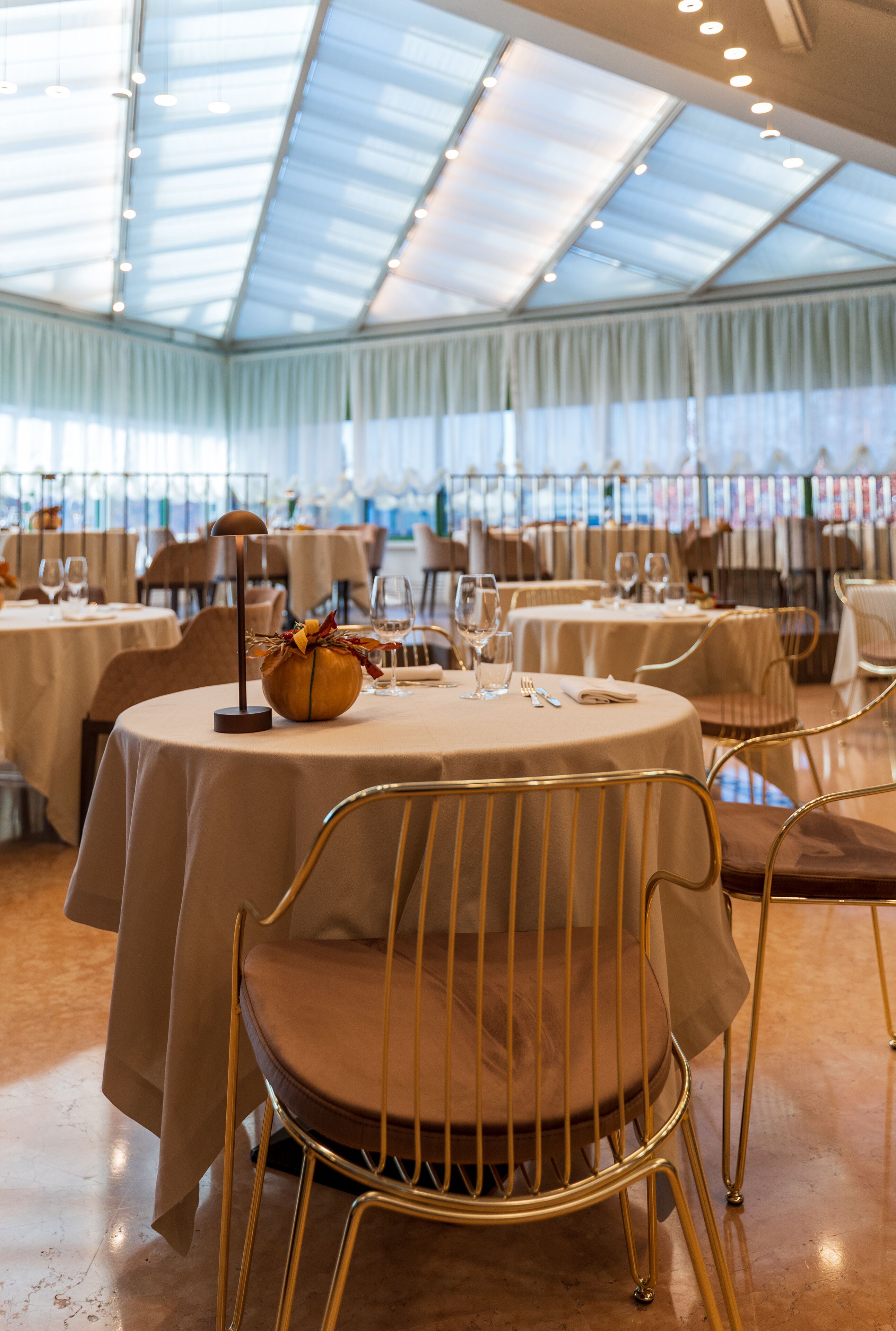 A restaurant with round tables, gold chairs, and a glass ceiling.