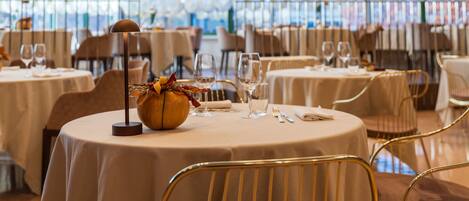 A restaurant with round tables, gold chairs, and a glass ceiling.
