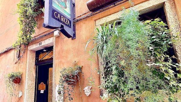 A building with a sign reading "CARIZA" and a door with a small window. There are plants growing on the walls and hanging from the window. - Ca' Riza (Venice)